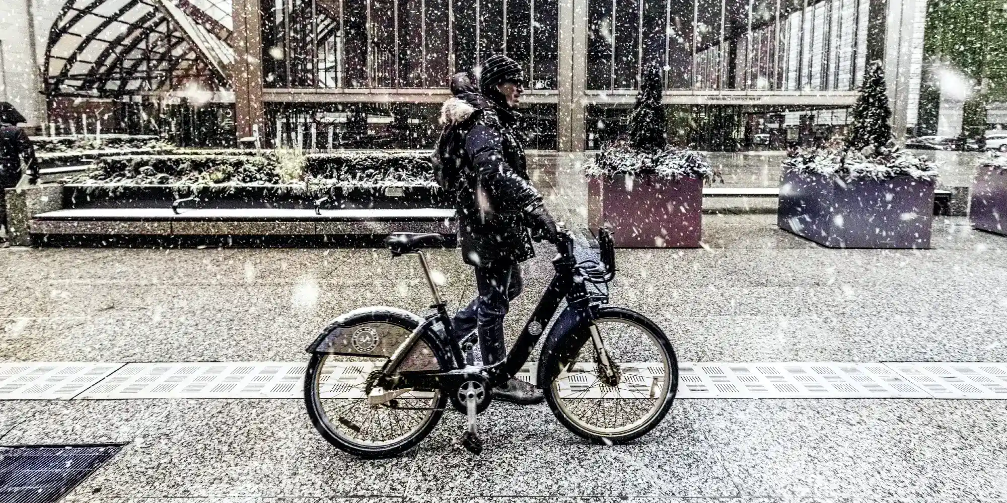in the city, a rider walks their ebike across a pedestrian mall in the middle of a snow flurry